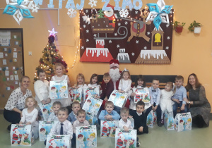 Dzieci z grupy Motylków z Mikołajem oraz otrzymanymi prezentami, w tle widać choinkę i zimową dekoracje